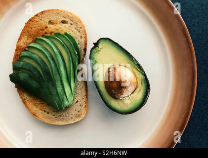 Avocado in Scheiben geschnitten auf Roggen Toast mit halben Avocado auf einer Platte Stockfoto
