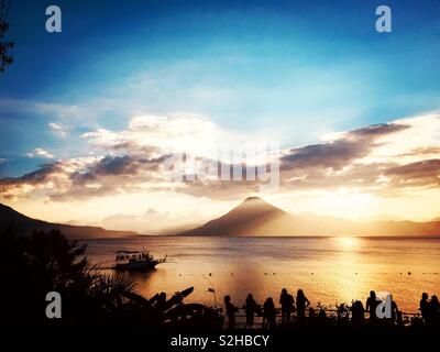 Silhouetted Touristen beobachten Sie den Sonnenuntergang über der Atitlan See & Vulkan San Pedro als Fähre Vergangenheit Kreuzfahrten, Guatemala, Mittelamerika Stockfoto