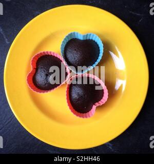 Drei herzförmige chocolate Cupcakes auf einem hellen Gelb Platte Stockfoto