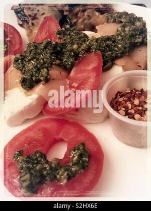 In der Nähe von Tomaten, Mozzarella, geräuchertem Lachs und Pesto mit einem Behälter mit rotem Pfeffer Flocken Stockfoto