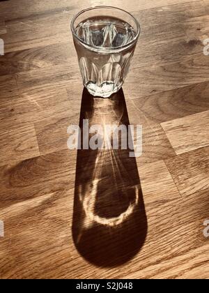 Glas Wasser wirft einen langen Schatten auf einem Tisch Stockfoto