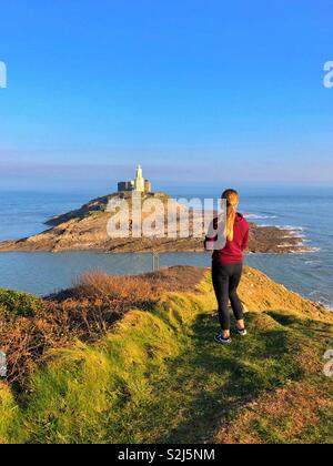 Junge Frau Richtung Mumbles Leuchtturm suchen, Mumbles Landspitze, Swansea, South West Wales, Februar. Stockfoto