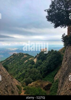 Blick von der Spitze des Berges Montserrat auf eine kleine Kapelle, die in den Felsen vor dem Hintergrund der Wolken und das Tal unter Stockfoto