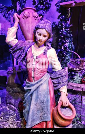 Emanuele Fontanini Erbstück Krippe Statue von Langhaarigen Frau im roten Kleid mit lila Schal und blauen Schürze tragen von Wasser in Krügen von Obst stehen in der Stadt von Bethlehem Stockfoto