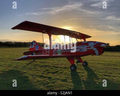 Doppeldecker bei Sonnenuntergang bei Sonnenuntergang auf dem Gras Flugplatz Stockfoto