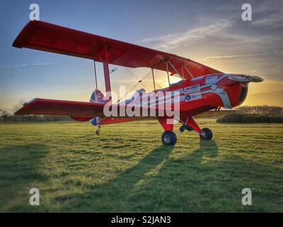 Doppeldecker bei Sonnenuntergang bei Sonnenuntergang auf dem Gras Flugplatz Stockfoto