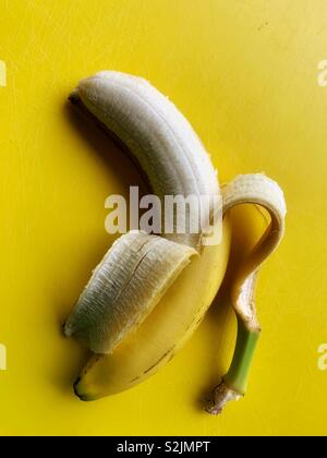 Eine einzelne geschält reife Banane auf einem hellen gelben Hintergrund Stockfoto