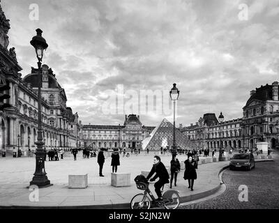 Ein Mann reitet ein Fahrrad und Touristen stehen in der Nähe des Louvre Pyramide am Eingang des Louvre in Paris, Frankreich Stockfoto