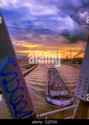 Großen Fluss transport Boot unter einer Brücke über den Fluss Schelde bei Sonnenuntergang mit den goldenen Glanz am Himmel unter den dunklen und blauer Himmel über Stockfoto