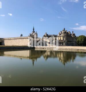 Blick auf Schloss Chantilly von über den großen Teich auf dem Gelände, die Gebäude im Wasser spiegelt Stockfoto