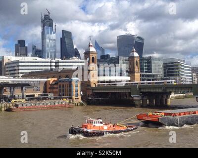 Ein Schlepper ziehen ein lastkahn entlang der Themse Vergangenheit Cannon Street Bahnhof mit der Stadt London, London, England, UK. Stockfoto