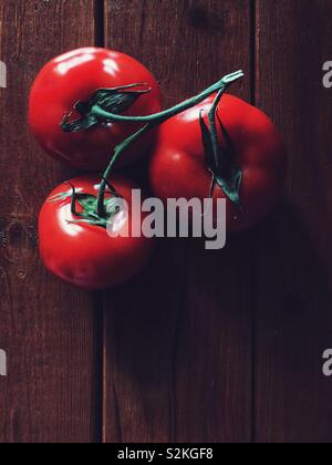 Drei rote Tomaten auf der Rebe auf einem braunen Holz- Oberfläche Stockfoto