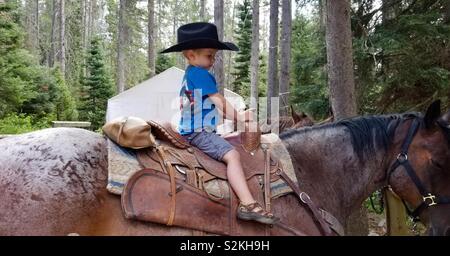 Junge tragen Cowboyhut auf Großvaters Pferd bei Mountain Camp sitzen Stockfoto