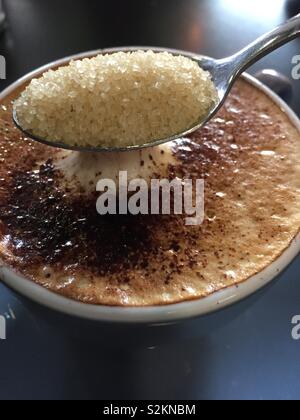 Einen Löffel voll Zucker schaumig Tasse Cappuccino, Nahaufnahme hinzugefügt werden. Vertikale Hintergrund closeup schaumigen Milch trinken in Becher mit Schokolade bestreut auf der Oberseite Stockfoto