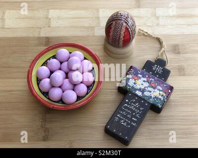 Ostern mit einem Ei, ein Holzkreuz und eine keramische Schüssel mit rosa Pralinen Stockfoto