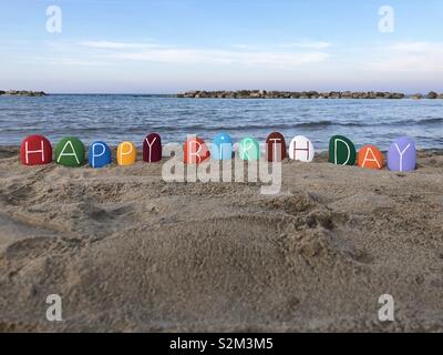 Happy Birthday, kreative Nachricht mit bunten Steinen über den Strand mit Meer Hintergrund Stockfoto