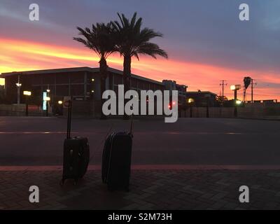 LOS ANGELES, Ca, APRIL 2019: zwei Koffer an leeren Straßenkante, Patsouras Transit Plaza außerhalb der Union Station in der Innenstadt. Kurz vor Sonnenaufgang mit Silhouette Palmen und Orange Sky Stockfoto