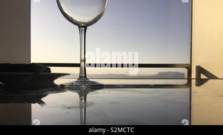 Unten Glas Wein auf reflektierenden Tabelle am späten Nachmittag mit Berge in der Ferne sichtbar durch Fenster Stockfoto