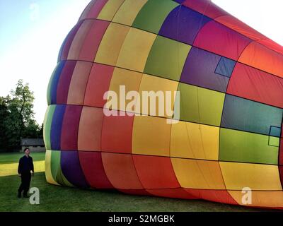 Farbenfroher Heißluftballon mit Regenbogen, der auf dem Boden liegt und sich mit heißer Luft füllt, um den Flug vorzubereiten, Schottland, Großbritannien Stockfoto