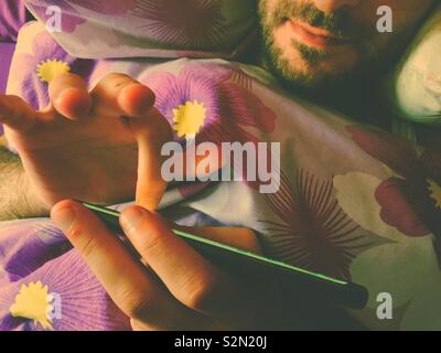 Mann mit Smart Phone im Bett Stockfoto