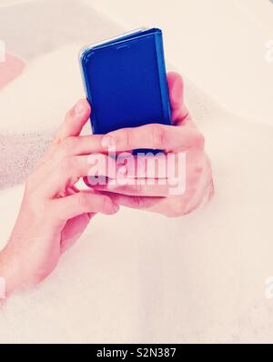 Des Menschen Hände halten Smartphone in Badewanne Stockfoto