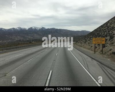 Fahrt nach Westen auf der Autobahn 15 Freeway durch die Berge bei San Bernardino National Forest, Kalifornien. Bewölkten Tag. Gelbe runaway Lkw Rampe Zeichen an der Seite Stockfoto