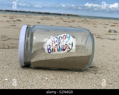 Alles Gute zum Geburtstag Nachricht geschnitzt und auf einem Stein in einem Glas mit Sand am Strand farbige Stockfoto