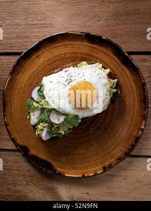 Avocado Toast mit sunny side up Ei auf braun Teller zum Frühstück Stockfoto