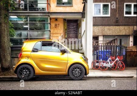 Ein gold Smart Auto in einer Straße im Londoner Stadtteil Notting Hill geparkt und zwei Fahrräder sind im Hintergrund zu sehen und lehnte sich gegen einige Geländer Stockfoto