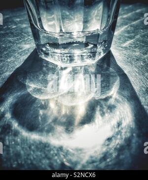 Zusammenfassung von teilweise vollen Glas Wasser auf der sonnenbeschienenen Terrasse Tisch aus Metall mit Lichtbrechung Muster und Schatten. Stockfoto