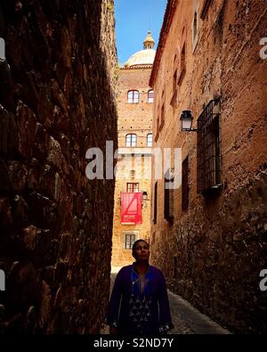 Eine Frau geht in einer engen Straße in die Vorderseite von Turm des Toledo-Moctezuma Palace in der mittelalterlichen Stadt von Caceres, Extremadura, Spanien Stockfoto