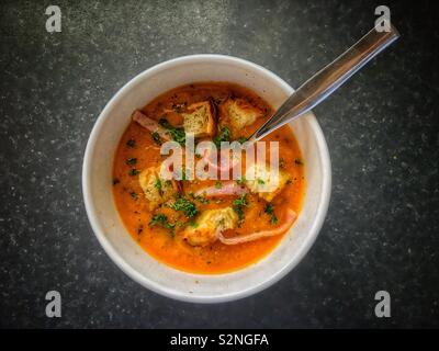 Eine Schüssel mit Karotte und Koriander Suppe mit Croutons, Speck und Petersilie. Stockfoto