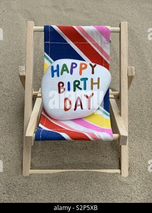 Alles Gute zum Geburtstag aus Stein auf einem bunten Chaiselongue über den Sand Stockfoto