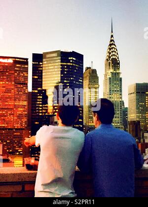 Zwei Männer, die den Blick auf Midtown Manhattan Wolkenkratzer, der bei Dämmerung von einer Dachterrasse in Murray Hill, New York, USA Stockfoto