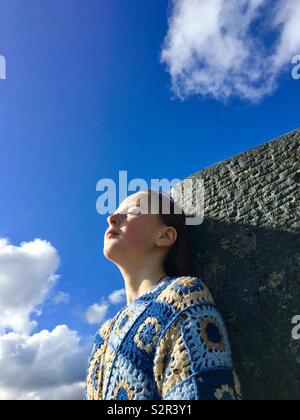 Ein junges Mädchen mit geschlossenen Augen gegen eine flache Rock mit blauem Himmel in einem Boden zurück gelehnt Stockfoto