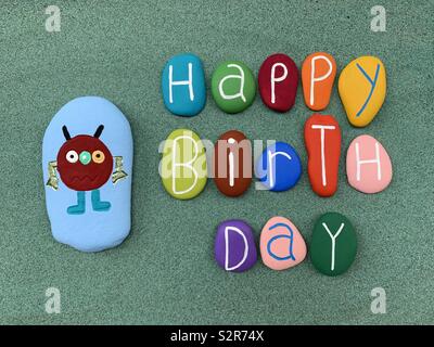 Happy Birthday mit Kreativen und bunten Steinen über grünen Sand Stockfoto
