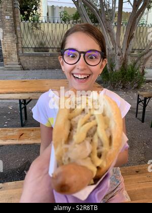 Glückliches Kind Mädchen suchen an einer deutschen Wurst mit Sauerkraut Stockfoto