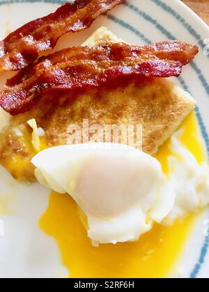 Köstliches Frühstück mit runny pochierte Eier mit Kartoffeln Kuchen und knusprigen Bauchspeck Speck serviert Stockfoto