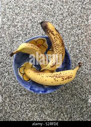 Drei reife Bananen in einem blauen und gelben Schüssel auf strukturierte Oberfläche Stockfoto