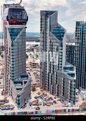 Greenwich, Großbritannien - 5. Juli 2019: Emirates Air line Seilbahn Kabine fährt vorbei an spektakulären Hochhäusern auf der Greenwich Peninsula. Stockfoto