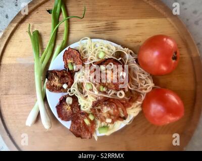 Gebratene Tomaten und gehackte Zwiebeln auf einem Teller Spaghetti Nudeln. Stockfoto