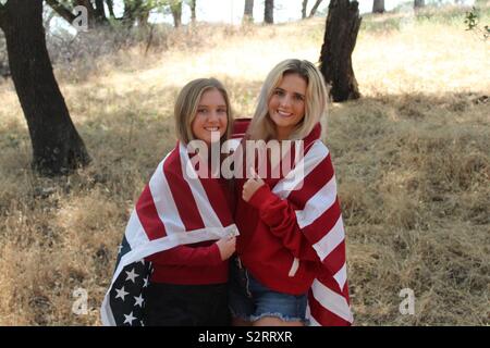 Zwei schöne blonde Mädchen drapiert in eine amerikanische Flagge in den Wald zur Feier des vierten Juli - Tag der Unabhängigkeit USA, Nordamerika Stockfoto