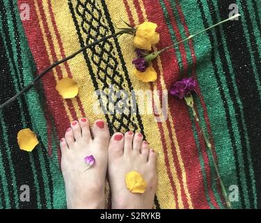 Blumen und Rosenblätter auf die Füße der Frau stehen auf einem farbenfrohen roten, grünen und gelben Decke - Füße und Blumen Stockfoto