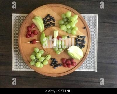 Einen leckeren Teller mit Obst und eine Frucht kabob auf hölzernen Serviertablett - Blaubeeren, Himbeeren, Äpfel und Trauben. Stockfoto