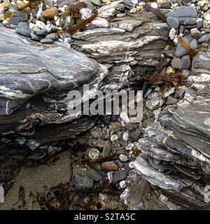 Bunte Felsen und Kieselsteine mit Algensträngen am Rande eines Strandfelsenpools. Mobiltelefon-Foto mit einem Telefon oder Tablet Nachverarbeitung. Stockfoto