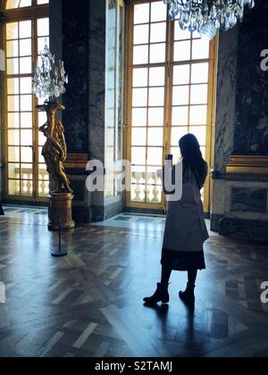 Junge Frau mit Foto auf Ihrem Telefon im Spiegelsaal im Schloss von Versailles Stockfoto