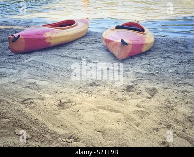 Pulsierende rosa und gelb Kajaks auf dem leeren Sandstrand von Abdrücken und von Wasser umgeben Stockfoto