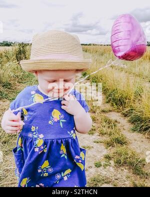 1-Jähriges Mädchen läuft in einem Feld mit einem Rosa Ballon Stockfoto