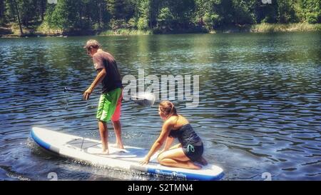 Junge und Mädchen Teenager auf einem Paddle Board im See unter den Wald Stockfoto
