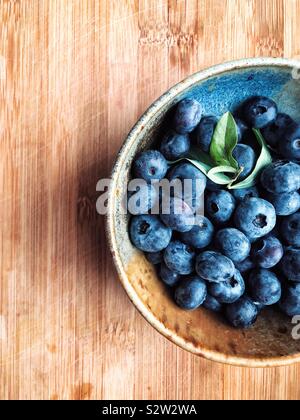 Frische Heidelbeeren im modernen Steinzeug Schüssel auf Bambus board Stockfoto